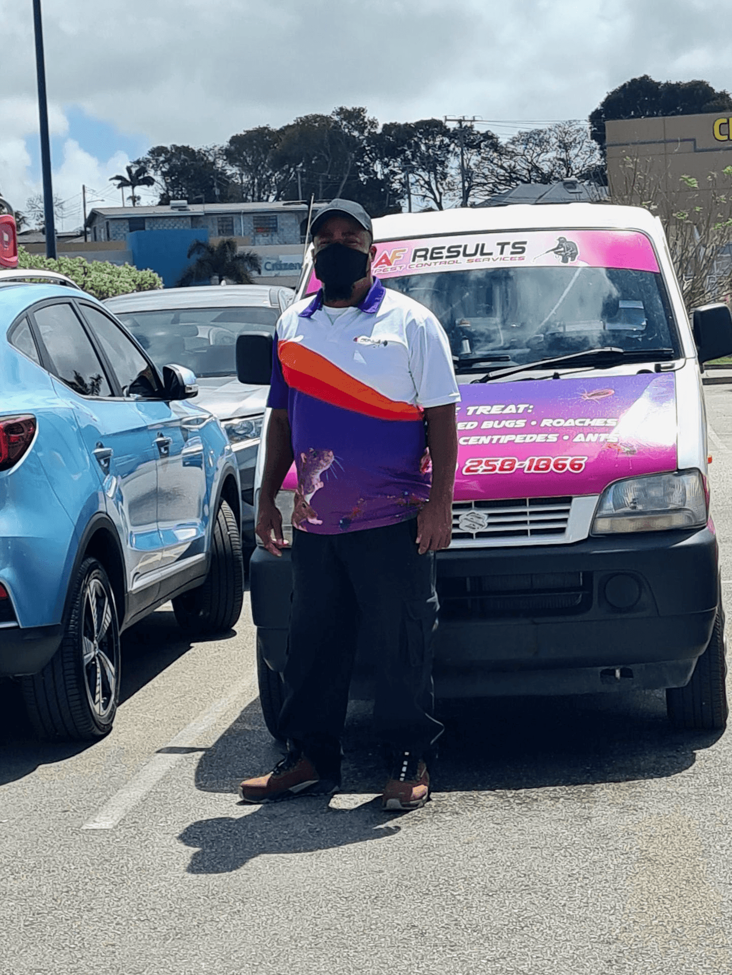 Person standing in front of a pest control service van with blue and other cars parked nearby.